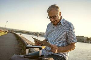 mayor hombre leyendo un mapa fuera de con un maleta. turista concepto foto