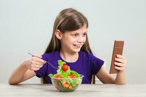 A girl choosing between salad and a chocolate bar photo
