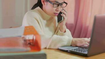 joven asiático mujer utilizando teléfono inteligente y trabajando sentado en oficina a hogar de cerca. video