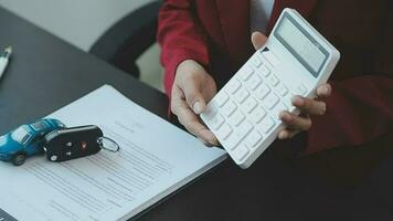 Closeup of Asian female signing car insurance document or lease paper contract or agreement. Buying or selling new or used vehicle with car keys on table. video