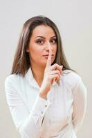 A woman in a white shirt making a silence gesture photo