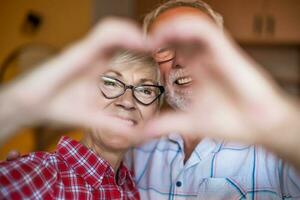 A senior couple makes a heart sign with their hands photo