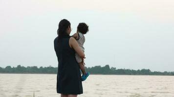famille content, mère et bébé Faire Extérieur Activités sur le rive de une Lac à le coucher du soleil dans été. video