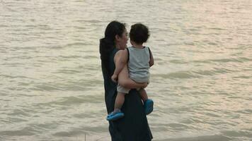 Family happy, Mother and baby doing outdoor activities on the shore of a lake at sunset in summer. video