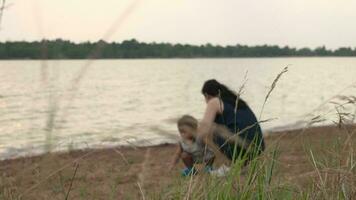 familia feliz, madre y bebé haciendo al aire libre ocupaciones en el apuntalar de un lago a puesta de sol en verano. video