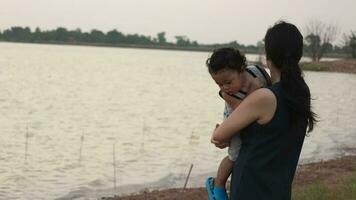 familie Vrolijk, moeder en baby aan het doen buitenshuis activiteiten Aan de kust van een meer Bij zonsondergang in zomer. video