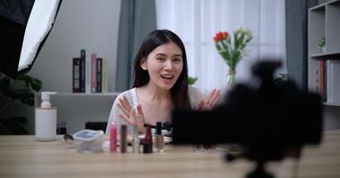 Footage of Beautiful asian woman blogger is showing how to makeup and use cosmetics. In front of the camera to record vlog video live streaming at home. Influencer and cosmetics concepts.