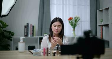 Handheld shot, Beautiful asian woman blogger is showing how to makeup and use cosmetics. In front of the camera to record vlog video live streaming at home. Influencer and cosmetics concepts.