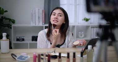 Handheld shot, Beautiful asian woman blogger is showing how to makeup and use cosmetics. In front of the smartphone to record vlog video live streaming at home. Influencer and cosmetics concepts.