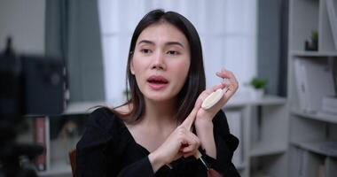 Handheld shot, Beautiful asian woman blogger is showing how to makeup and use cosmetics. In front of the smartphone to record vlog video live streaming at home. Influencer and cosmetics concepts.