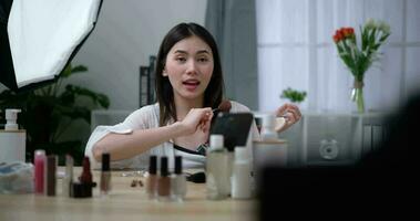 imágenes de hermosa asiático mujer blogger es demostración cómo a maquillaje y utilizar productos cosméticos. en frente de el cámara a grabar vlog vídeo En Vivo transmisión a hogar. hombre de influencia y productos cosméticos conceptos. video
