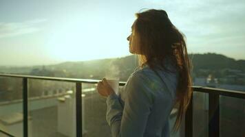 mooi vrouw drankjes kop van koffie of thee, aan het kijken een mooi stedelijk visie en genieten kom tot rust ademen vers bevriezing lucht Aan balkon Bij dageraad video