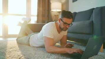 Man with glasses is lying on the floor, working on a laptop. Concept of remote work video