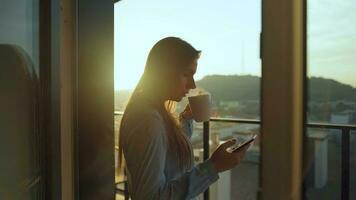 jolie femme les boissons tasse de café ou thé, en train de regarder une magnifique Urbain vue et prendre plaisir se détendre respiration Frais gelé air sur balcon à Aube video