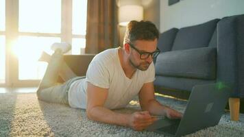 uomo con bicchieri è dire bugie su il pavimento, Lavorando su un' il computer portatile. concetto di a distanza opera video