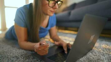 femme avec des lunettes est mensonge sur le sol et fait du un en ligne achat en utilisant une crédit carte et portable. en ligne achats video