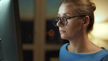 Woman in glasses looking on the monitor and surfing Internet at night. The monitor screen is reflected in the glasses. Work at night. Home Office. Remote work video