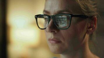 Woman in glasses looking on the monitor and surfing Internet at night. The monitor screen is reflected in the glasses. Work at night. Home Office. Remote work video