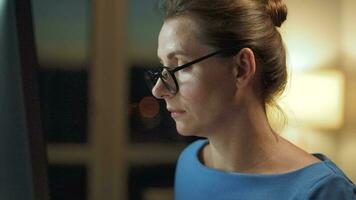 Woman in glasses looking on the monitor and surfing Internet at night. The monitor screen is reflected in the glasses. Work at night. Home Office. Remote work video