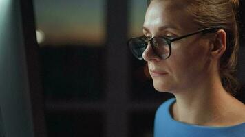 Woman in glasses looking on the monitor and surfing Internet at night. The monitor screen is reflected in the glasses. Work at night. Home Office. Remote work video