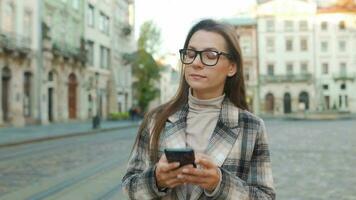 mujer caminando abajo un antiguo calle y utilizando teléfono inteligente video