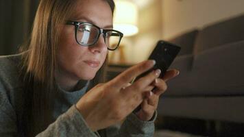 vrouw met bril is aan het liegen Aan de verdieping en gebruik makend van smartphone in de avond video