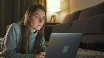 Woman is lying on the carpet and working on a laptop in the evening. Concept of remote work video