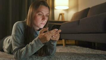 kvinna är liggande på de golv och använder sig av smartphone i de kväll video