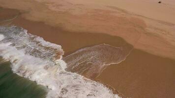 aéreo ver de zumbido volador encima mar, navegar, y agua estrellarse sobre el arenoso playa desde un parte superior ángulo video