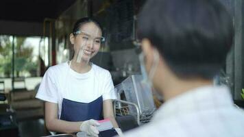 Young woman working in a coffee shop wearing a mask and gloves for cleaning Collect customer money by scanning QR codes with male customers.. video