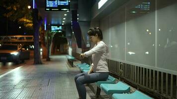 mujer en rutina de ejercicio ropa mirando a reloj a autobús detener a noche. video