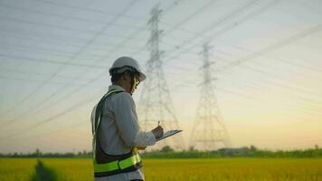 man wearing electrical engineer uniform to inspect high-voltage poles and take notes on the script to save the information. video