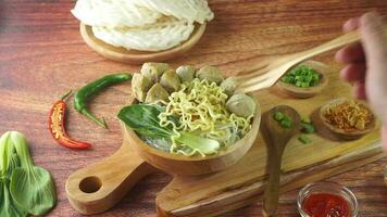 Meatball, in Indonesia known as Bakso or Baso. Served with noodles vegetables chili sauce in a bowl on wood background with hand. Close up top view flat lay copy space video