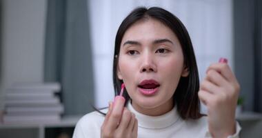 Handheld shot, Beautiful asian woman blogger is showing how to makeup and use cosmetics. In front of the smartphone to record vlog video live streaming at home. Influencer and cosmetics concepts.