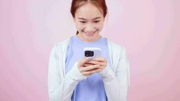 asiático mujer utilizando móvil teléfono texto charla en pie en camiseta en rosado antecedentes video