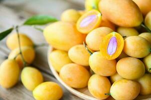 tropical Fruta nombre en Tailandia dulce amarillo mariano ciruela maprang plango o mayong niño, mariano ciruela Fruta y hojas en plato en de madera antecedentes foto