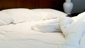 White mattress with blankets scattered. Three pillows lined up. Warm light in the bedroom. photo