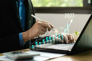 Businessman analyzes profits and plans 2023 business growth with virtual digital graphics. Positive indicators in 2023, businessman calculates financial data for long-term investments.Return on Stocks photo