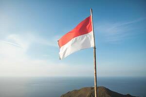 Indonesia national flag waving in the blue sky on the ocean background. Red and white flag with clouds. photo