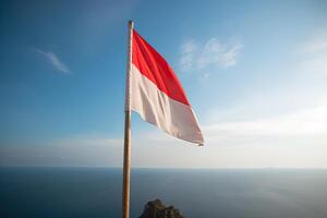 Indonesia national flag waving in the blue sky on the ocean background. Red and white flag with clouds. photo