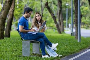 joven asiático y indio estudiante disfrutar teniendo relajante hora en el Universidad instalaciones mientras sentado y estudiando juntos en el banco durante el fin de semana concepto foto