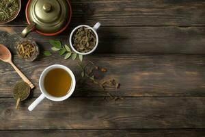 Cup of tea with teapot, organic green tea leaves and dried herbs on wooden table top view with copy space photo