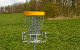 Disc Golf basket. Frisbee golf is sport and hobbie in outdoor park. Metal basket with chains for disc game surrounded by vibrant green trees. photo