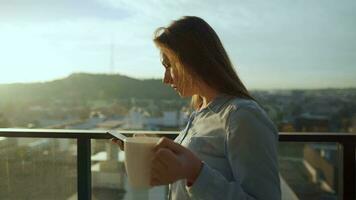jolie femme les boissons tasse de café ou thé, en train de regarder une magnifique Urbain vue et prendre plaisir se détendre respiration Frais gelé air sur balcon à Aube video