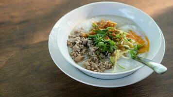 Minced Pork Congee with Egg on white bowl. Spoons are placed and plates are supported on a wooden table top. photo