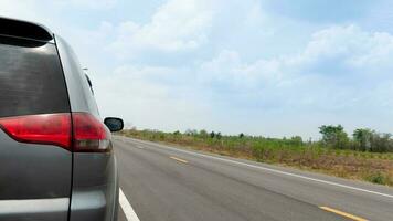 Rear side of gray car triving on the empty asphalt road. Beside with wide open spaces of provincial nature in Thailand. under blue sky and white clouds. photo