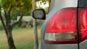 Rear side of gray car. covered with dew on the car. Background of garden blurred of tree and green grass. photo