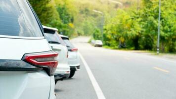 Beside of car parked in line on the side of the asphalt road. Beside view with green forest. Road winds up into a dense forest area. photo