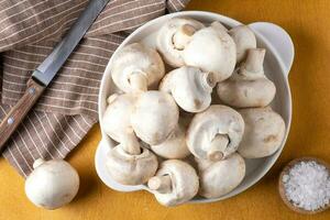 Champignon mushrooms on a white ceramic plate on a yellow background. photo