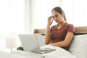 Young adult asian woman using laptop on bed for telemedicine mental health online therapy photo
